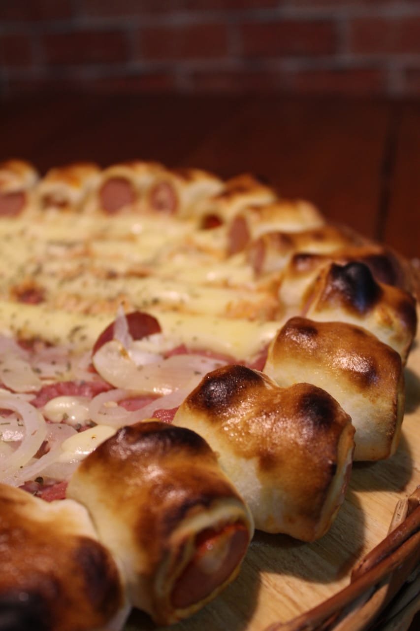 Detalhe da borda recheada dourada da pizza com parede de tijolos ao fundo