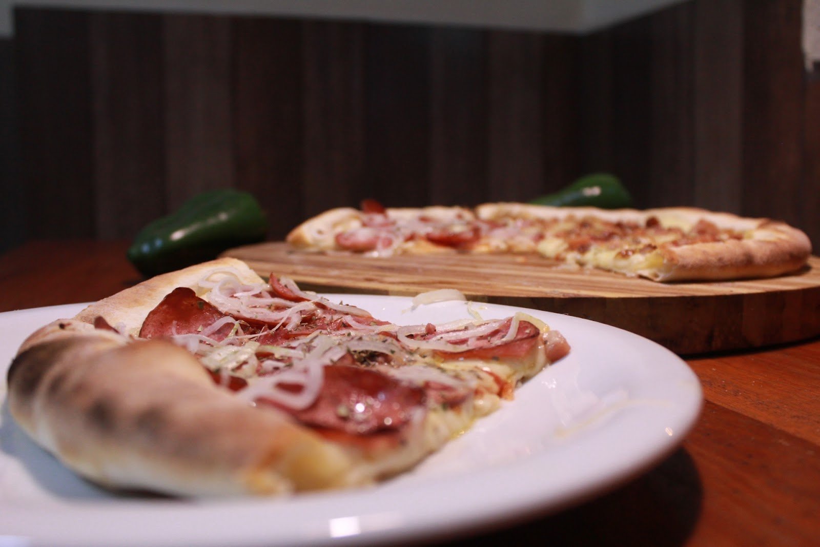 Duas pizzas de massa fina com calabresa e cebola servidas no prato e na tábua